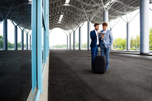 Foto grátis foto de dois jovens empresários falando no aeroporto e segurando o tablet