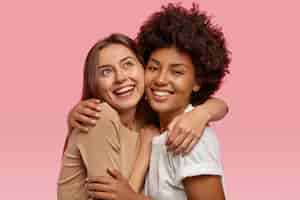 Foto grátis foto de duas mulheres alegres se abraçando e sorrindo positivamente, com expressões sonhadoras, demonstrando sentimentos verdadeiros