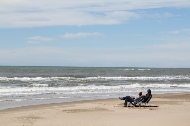 Foto de duas pessoas sentadas em cadeiras na praia, olhando para as ondas do mar e relaxando