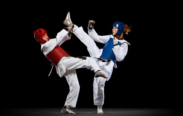 Foto de estúdio completa de duas mulheres, atletas de taekwondo treinando isolados sobre fundo preto