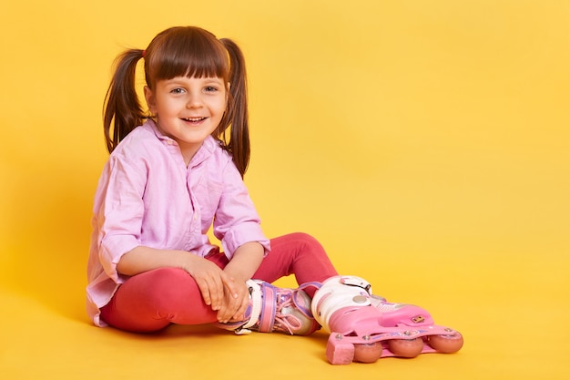 Foto de estúdio de cabelos escuros rindo menina com dois rabos de cavalo sentado