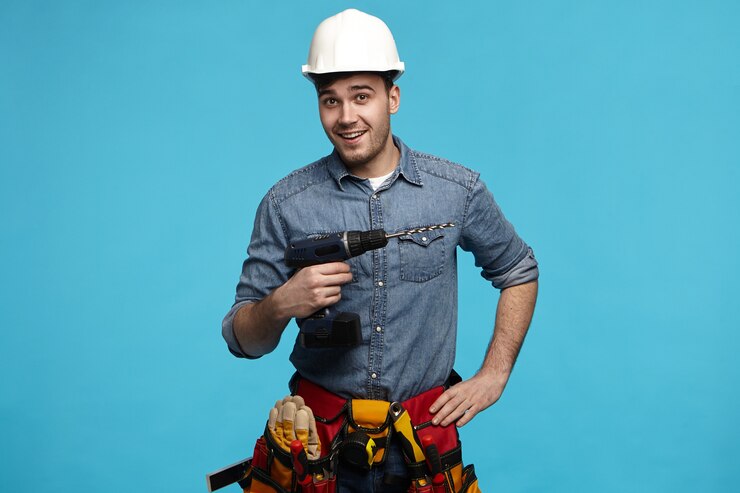 Foto grátis foto de estúdio de um jovem construtor amigável carregando a broca e o cinto com todos os instrumentos fazendo reformas para o cliente