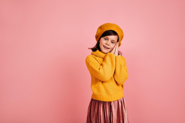 Foto de estúdio de uma criança bonita no suéter de malha Menina em êxtase em pé no fundo rosa