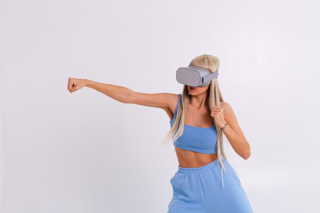 Foto de estúdio de uma jovem atraente em um terno azul quente da moda usando óculos de realidade virtual em uma luta de boxe