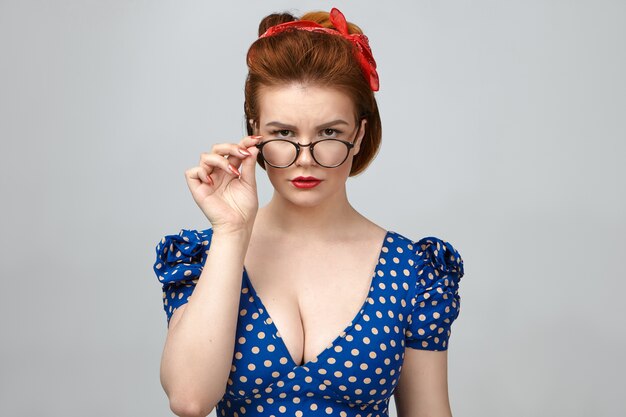 Foto grátis foto de estúdio de uma jovem e atraente professora caucasiana séria com roupa vintage, baixando os óculos elegantes e olhando para a câmera, posando isolada contra o fundo da parede em branco