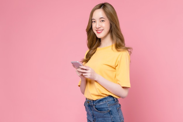 Foto de estúdio de uma linda mulher asiática segurando um smartphone e sorrindo sobre fundo rosa claro