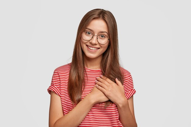 Foto de estúdio de uma mulher terna e amigável expressa um doce agradecimento, derrete-se com palavras agradáveis e mantém as mãos no plam