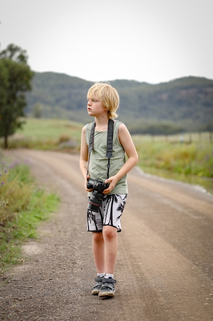 Foto de foco raso de um garotinho com uma câmera na estrada