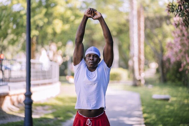 Foto de foco raso de um homem afro-americano com uma camisa branca se espreguiçando no parque