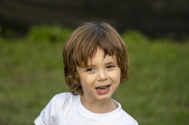 Foto de foco raso de um menino branco bonito e alegre ao ar livre