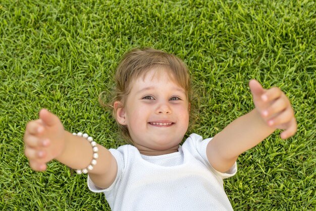 Foto de foco raso de uma jovem mulher deitada na grama verde e sorrindo para a câmera