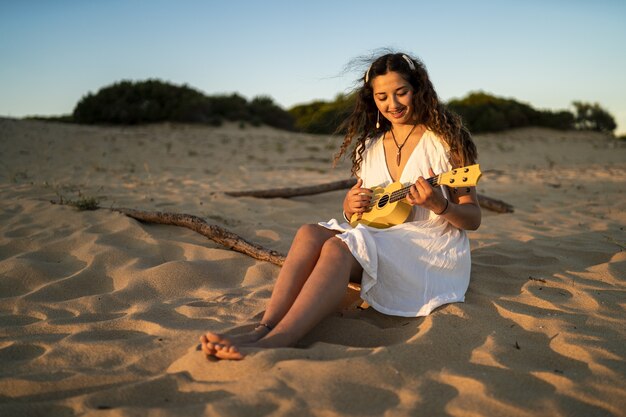 Foto de foco raso de uma mulher sorridente em um vestido branco sentada em um solo arenoso