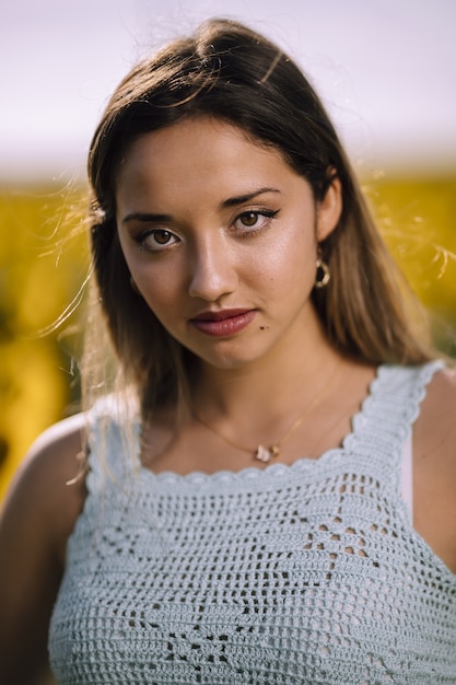 Foto de foco raso vertical de uma jovem mulher posando em um campo de girassóis brilhantes