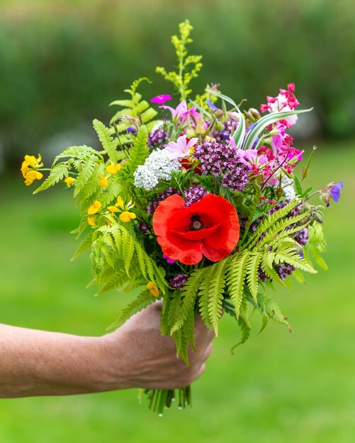 Foto de foco seletivo de alguém segurando um buquê de flores diferentes ao ar livre durante o dia