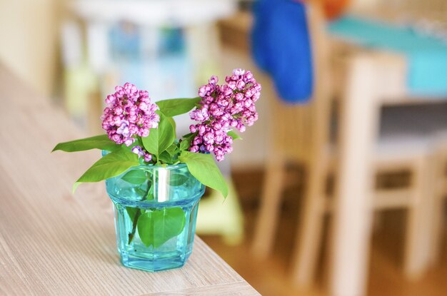 Foto de foco seletivo de galhos de flor lilás em um copo com água na mesa de madeira