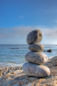 Foto de foco seletivo de pedras empilhadas em uma praia com um céu azul desfocado