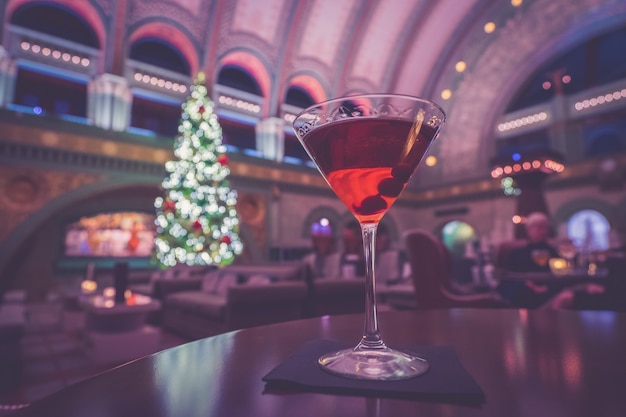 Foto de foco seletivo de um bom coquetel alcoólico com um bar noturno de Natal ao fundo