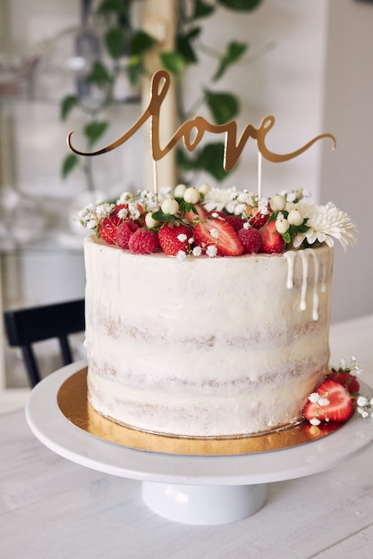 Foto de foco seletivo de um delicioso bolo de casamento branco com frutas vermelhas, flores e cobertura de bolo