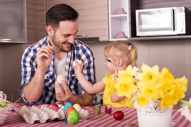 Foto de foco seletivo de um pai e uma filha felizes pintando ovos de Páscoa