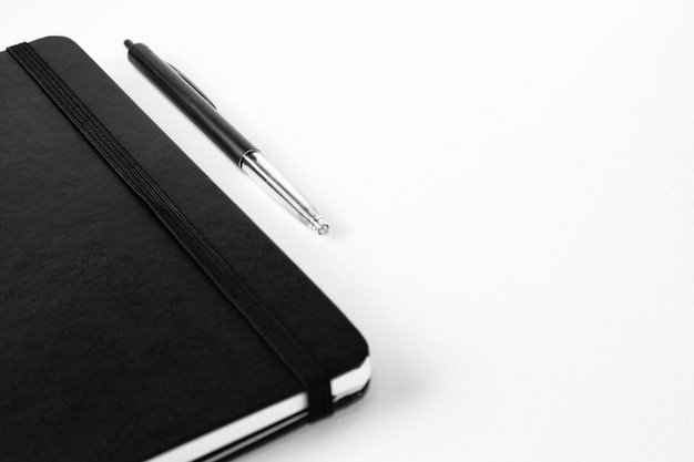 Foto de foco seletivo de uma caneta perto de um caderno em uma superfície branca