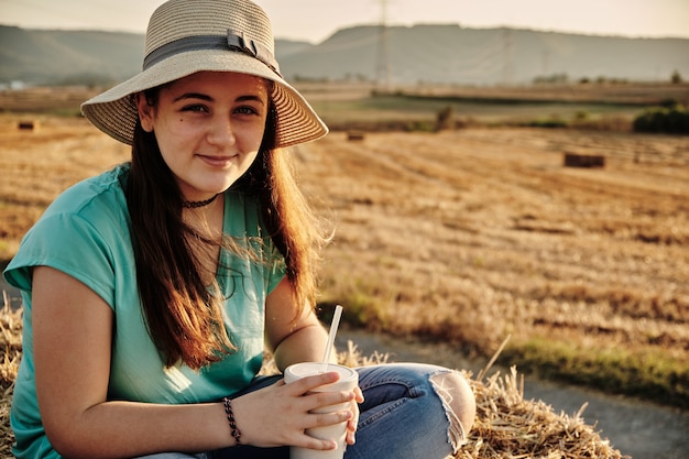 Foto de foco seletivo de uma jovem com chapéu redondo sentada e olhando para a câmera