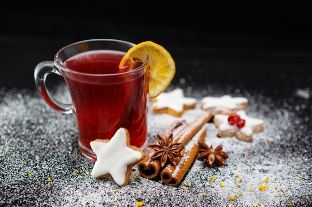 Foto de foco seletivo de uma xícara de chá com biscoitos deliciosos, estrelas de anis e paus de canela