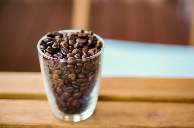 Foto de foco seletivo vertical de grãos de café em um copo transparente sobre uma mesa de madeira