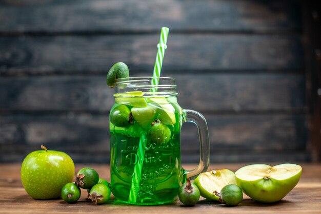 Foto de frente com suco de feijoa fresco dentro da lata com maçãs verdes na foto escura da bebida colorida