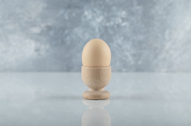 Foto de grande angular de ovo cozido em taça para ovo de madeira em fundo branco.