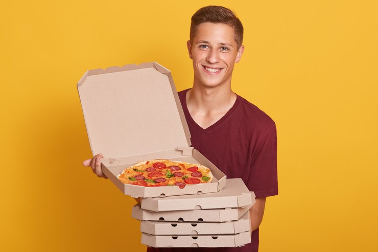 Foto grátis foto de homem alegre feliz vestindo camiseta casual de borgonha, olhando sorrindo para a câmera e segurando caixas de pizza