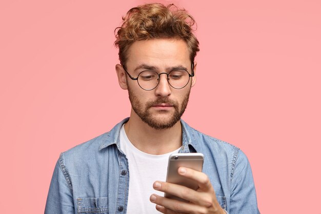 Foto de homem bonito com cabelo encaracolado, segura um celular moderno, digita mensagem de texto, recebe notificação