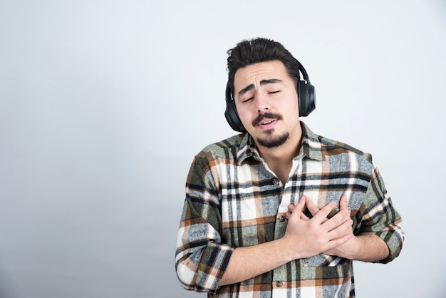 Foto de homem bonito com fones de ouvido, segurando-se sobre uma parede branca.