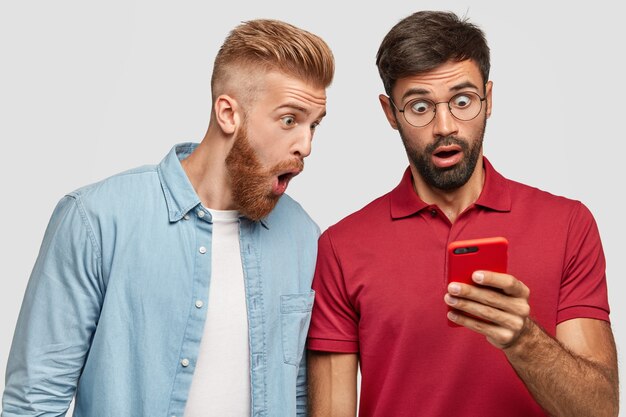 Foto de homens com a barba por fazer espantados e surpresos olhando para a tela do telefone inteligente