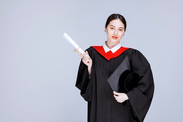 Foto de jovem estudante com certificado de faculdade em pé no estúdio. Foto de alta qualidade