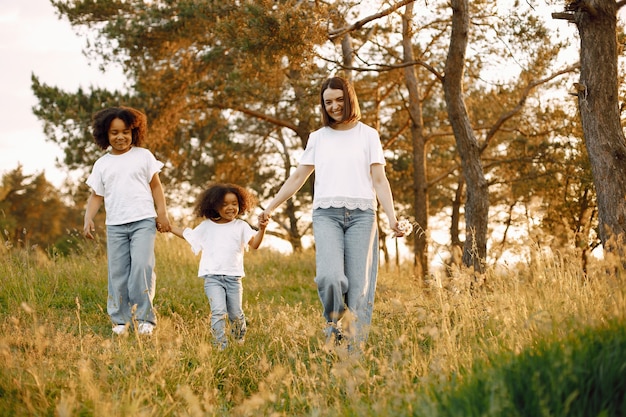 Foto de mãe caucasiana e duas filhas dela afro-americanas caminhando junto ao ar livre. meninas e mãe segurando as mãos uma da outra