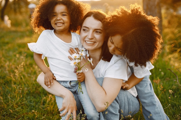 Foto de mãe caucasiana e duas filhas dela afro-americanas se abraçando junto ao ar livre. as meninas têm cabelo preto cacheado