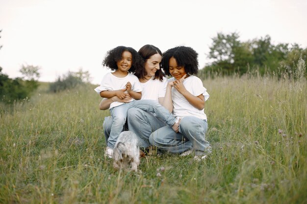 Foto de mãe caucasiana e duas filhas dela afro-americanas se abraçando junto ao ar livre. Menina com cabelo preto cacheado