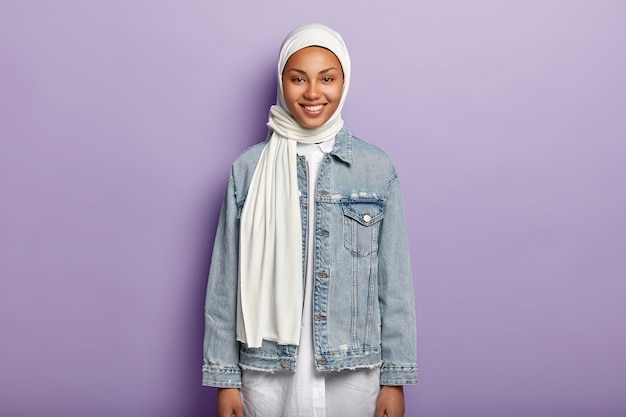 Foto de meio comprimento de uma mulher árabe feliz usando hijab branco, jaqueta jeans