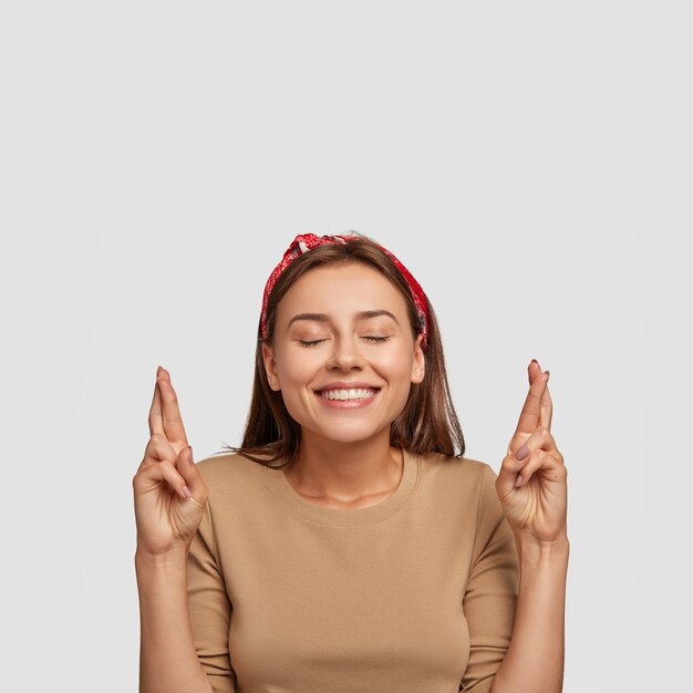 Foto de menina alegre satisfeita com sorriso amigável, mantém os olhos fechados de prazer