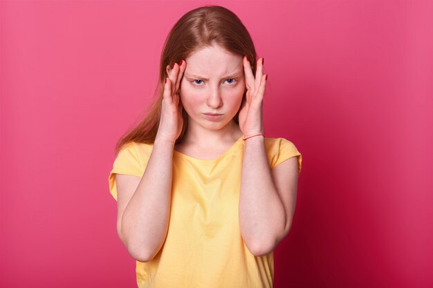 Foto de metade do comprimento da menina adolescente triste com dor de cabeça terrível, tem sérios problemas na escola, veste casualmente, posando em rosa. Expressões faciais e conceito de emoções de pessoas.