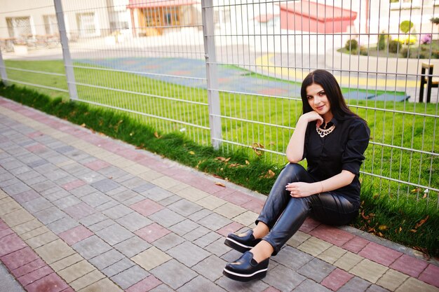 Foto de moda ao ar livre de uma linda mulher sensual com cabelos escuros em roupas elegantes, sentada contra a cerca de ferro na cidade do outono