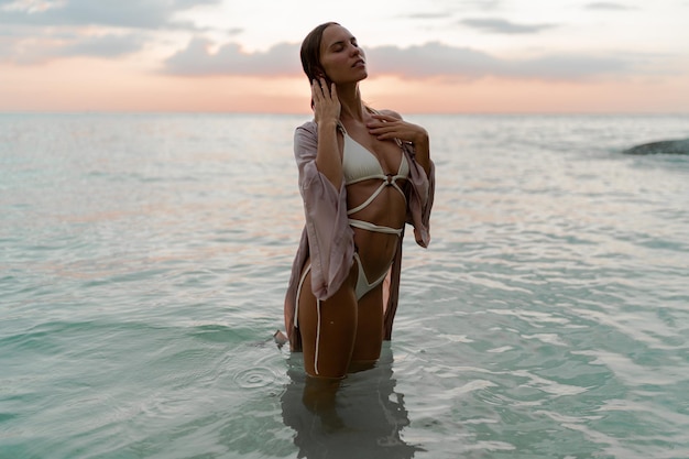 Foto de moda do modelo sedutor com corpo perfeito posando na praia tropical. Colos do pôr do sol.