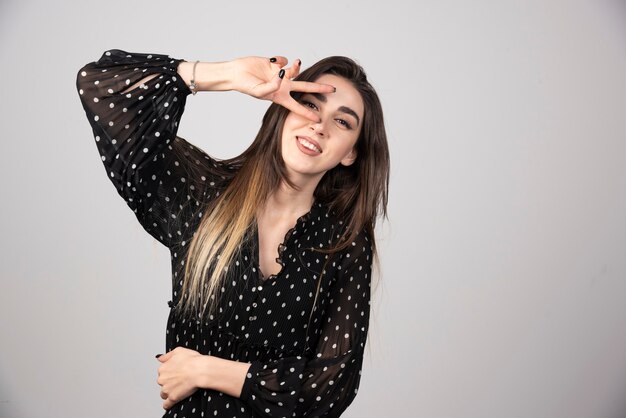 Foto de mulher jovem com vestido sorrindo e mostrando o símbolo da paz.