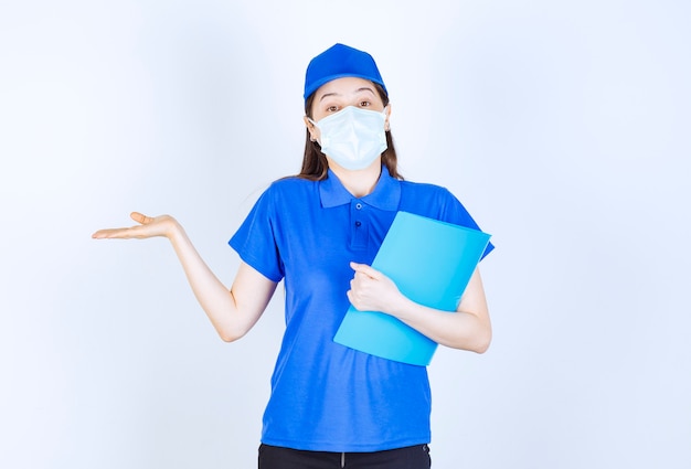 Foto de mulher jovem de uniforme, usando máscara médica e segurando uma pasta.