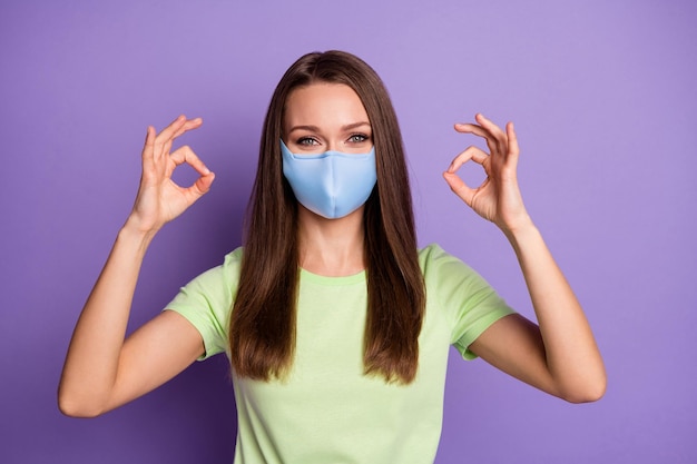 Foto de mulher mostrando dois sinais de ok usando máscara respiratória isolada em um fundo de cor violeta viva Foto Premium