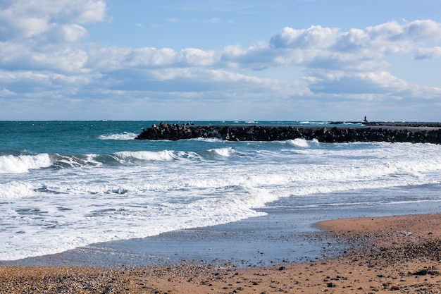 Foto de ondas relaxantes do mar na costa com doca de pedra sob céu nublado