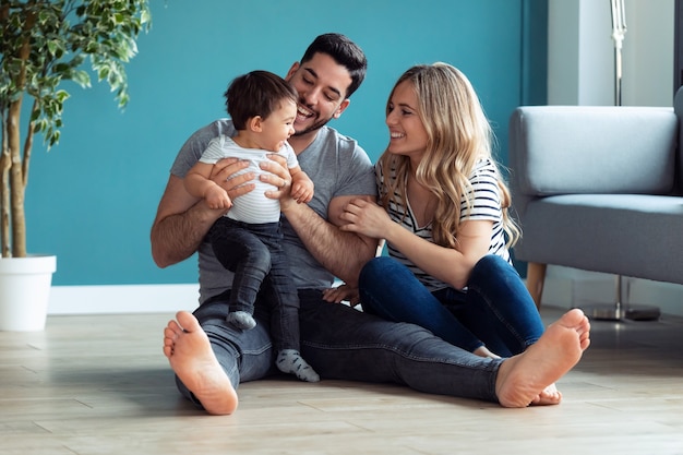 Foto de pais muito jovens brincando com o filho bebê enquanto está sentado no chão em casa.