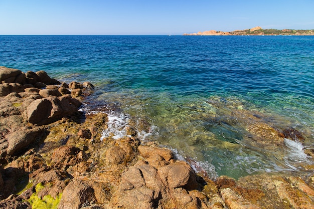 Foto de paisagem de grandes rochas, colinas verdes em um oceano azul com um céu azul claro