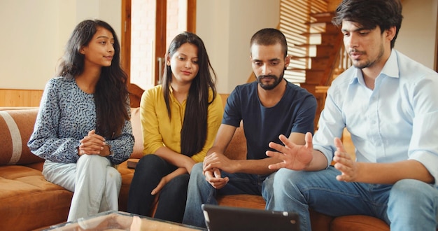Foto de quatro jovens amigos do sul da Ásia na Índia sentados dentro de casa e olhando para um tablet