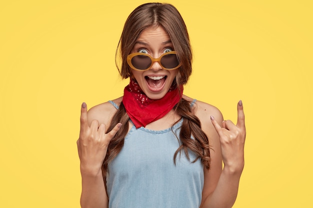 Foto de rosto de uma mulher hippie provocante e descolada mostra gesto de rock n roll com a mão exclamando em voz alta